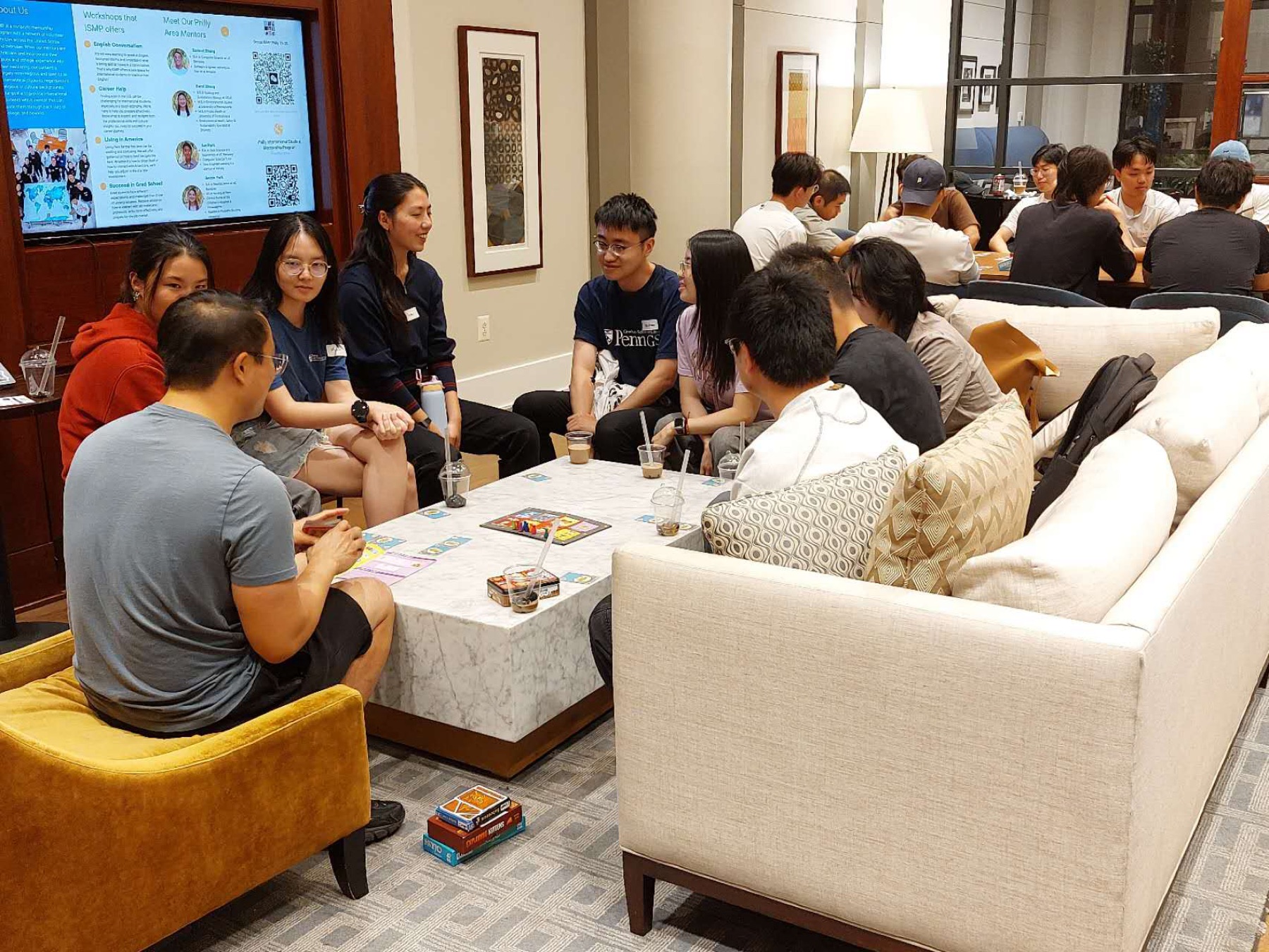 ISMP students and mentors sitting and talking together in a lounge, with a workshop slide on the screen behind them